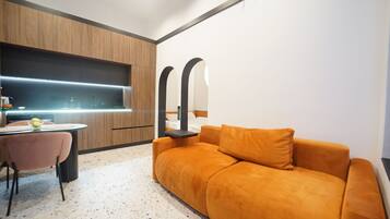 A modern living room with a sofa, a dining table, and a kitchen area with a built-in oven.