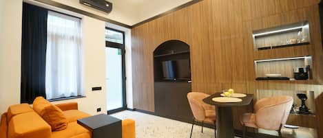 A modern living room with a sofa, a dining table with chairs, a TV, and built-in shelves.