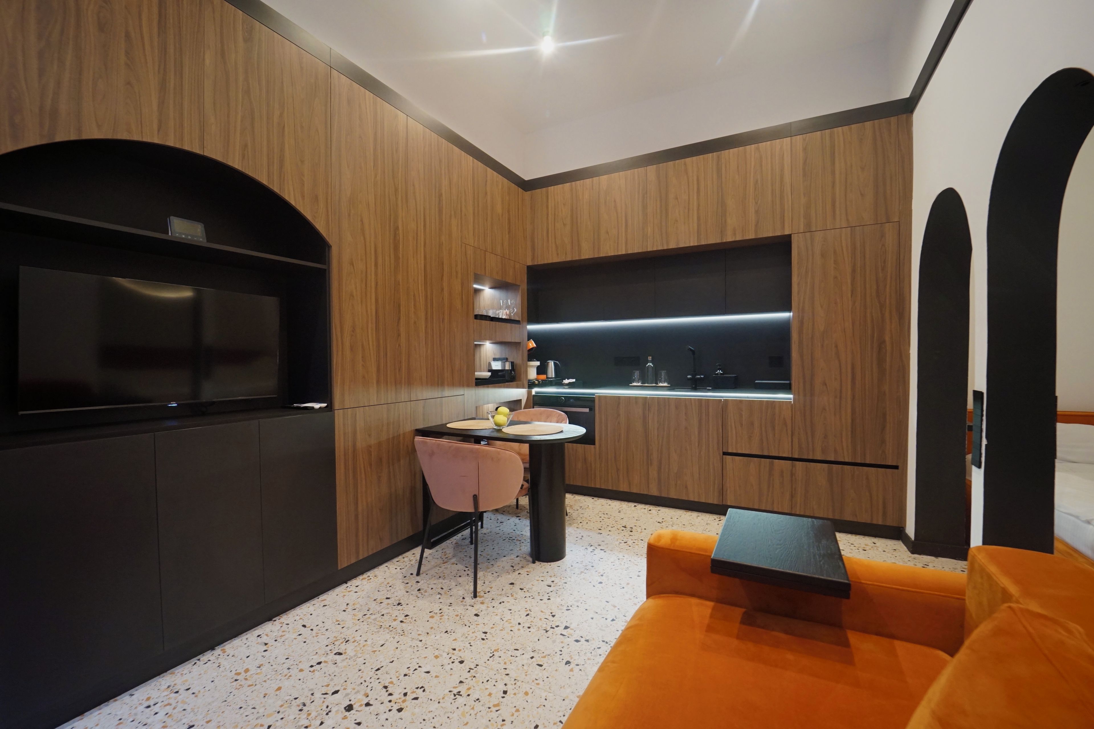 A modern kitchen with wooden cabinetry, a built-in oven, and a dining area with a pink chair and table.