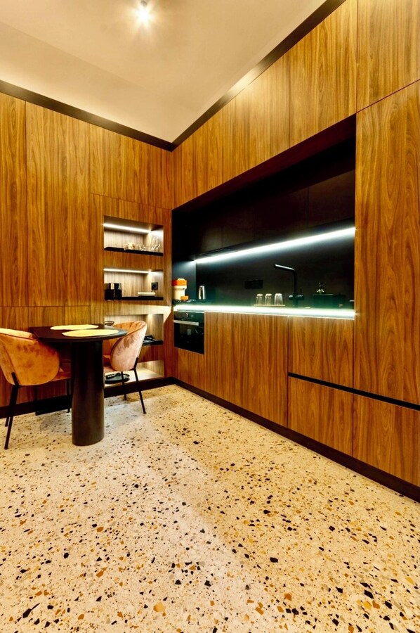 A modern kitchen with wooden cabinetry, a built-in oven, and a dining area with a table and chairs. - Jais Home-moon Apartment-muzeului Square-old Town (Cluj-Napoca)