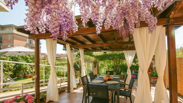 An outdoor patio with a wooden pergola, white curtains, and a table set for dining. - 2 bedroom gorgeous apartment in Marina di Massa (Marina di Massa)