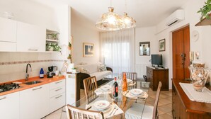 A modern kitchen with white cabinets, a dining table set for four, and a living area with a sofa and TV. - 2 bedroom gorgeous apartment in Marina di Massa (Marina di Massa)