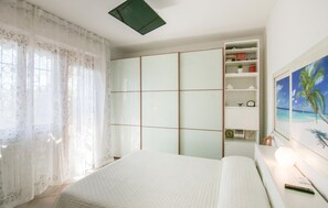 A bedroom with a bed, a wardrobe, a shelf with books and a clock, and a painting of a beach. - 2 bedroom gorgeous apartment in Marina di Massa (Marina di Massa)