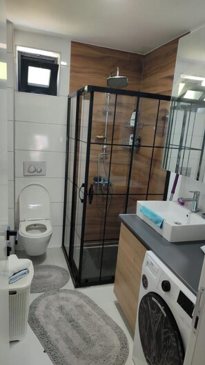 A modern bathroom with a toilet, shower enclosure, sink, and washing machine. - Tivat Terrace Suites (Tivat)