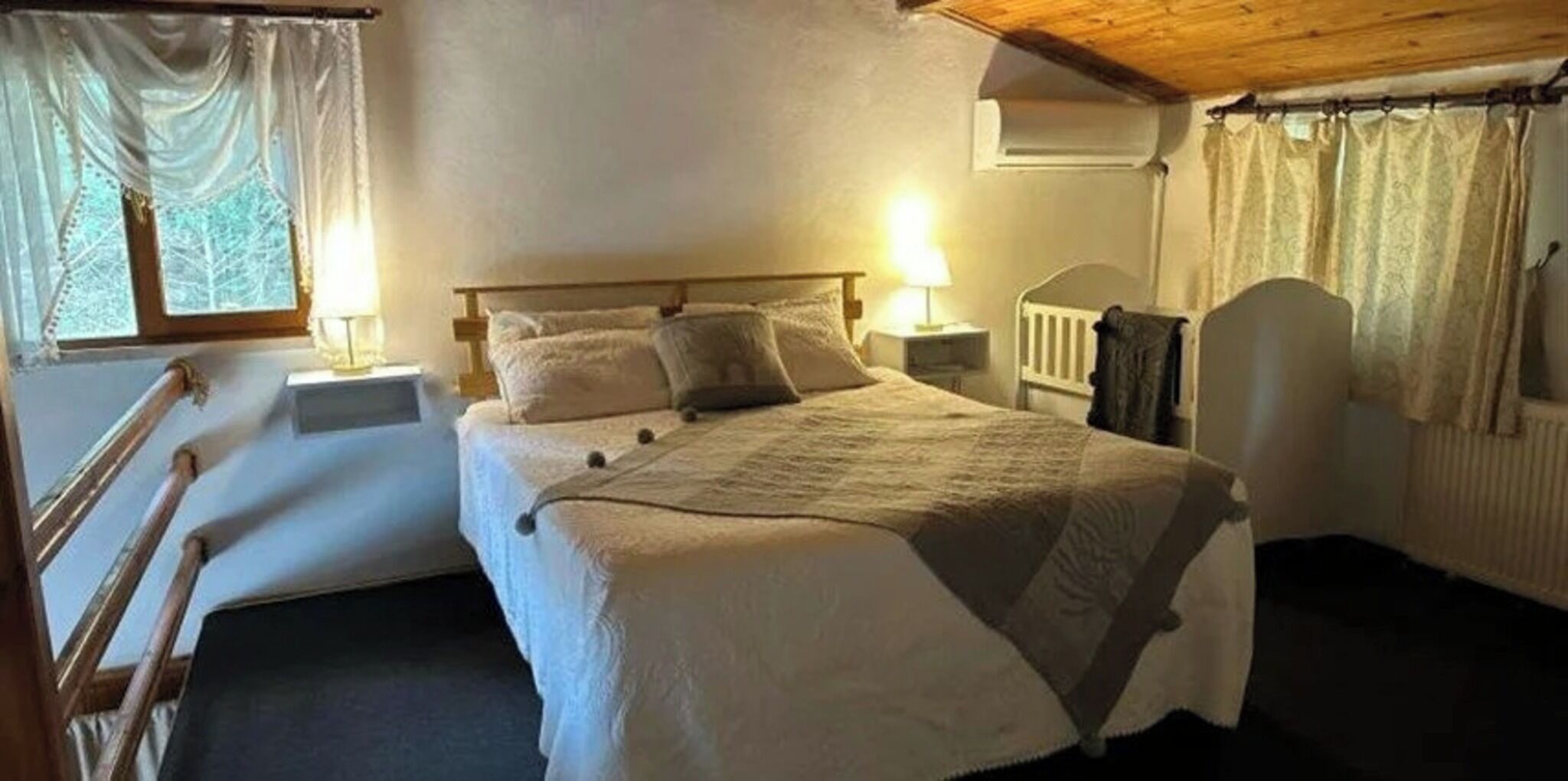 A bedroom with a bed, two bedside tables, a chair, a window with curtains, and a radiator.