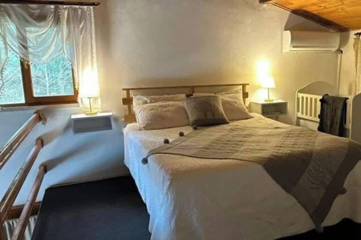Un dormitorio con una cama, dos mesitas de noche, una silla, un ventanal con cortinas y un radiador.