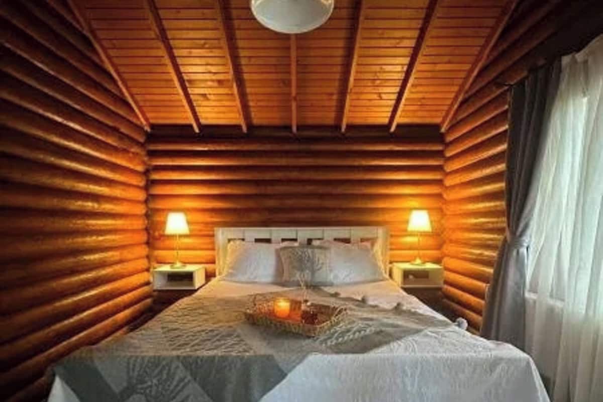 Un dormitorio de estilo cabaña con una cama, dos lámparas de noche, una lámpara colgante y una ventana con cortinas.