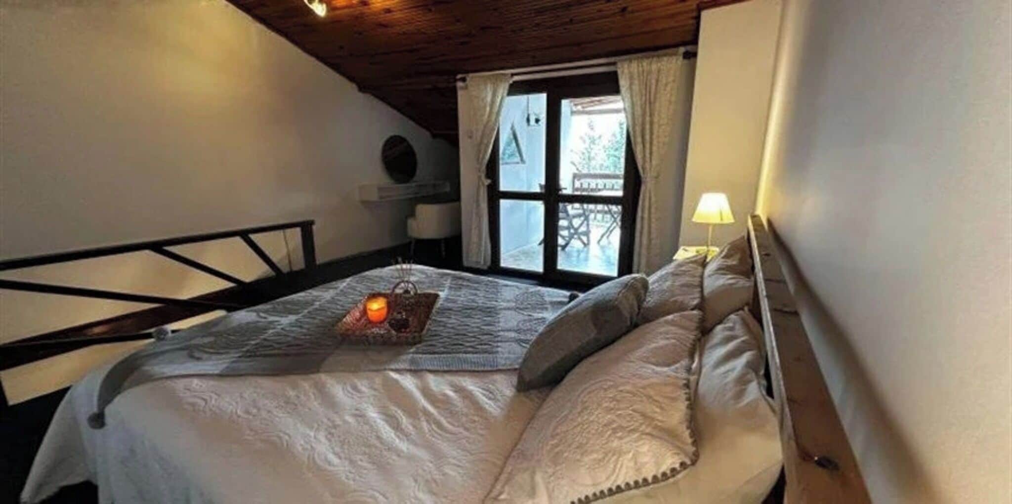 A bedroom with a bed, a window with curtains, a bedside lamp, and a small table with a tray.