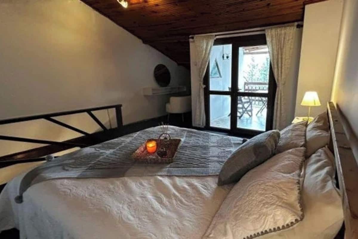 Un dormitorio con cama, ventana con cortinas, lámpara de noche y una mesita con bandeja.