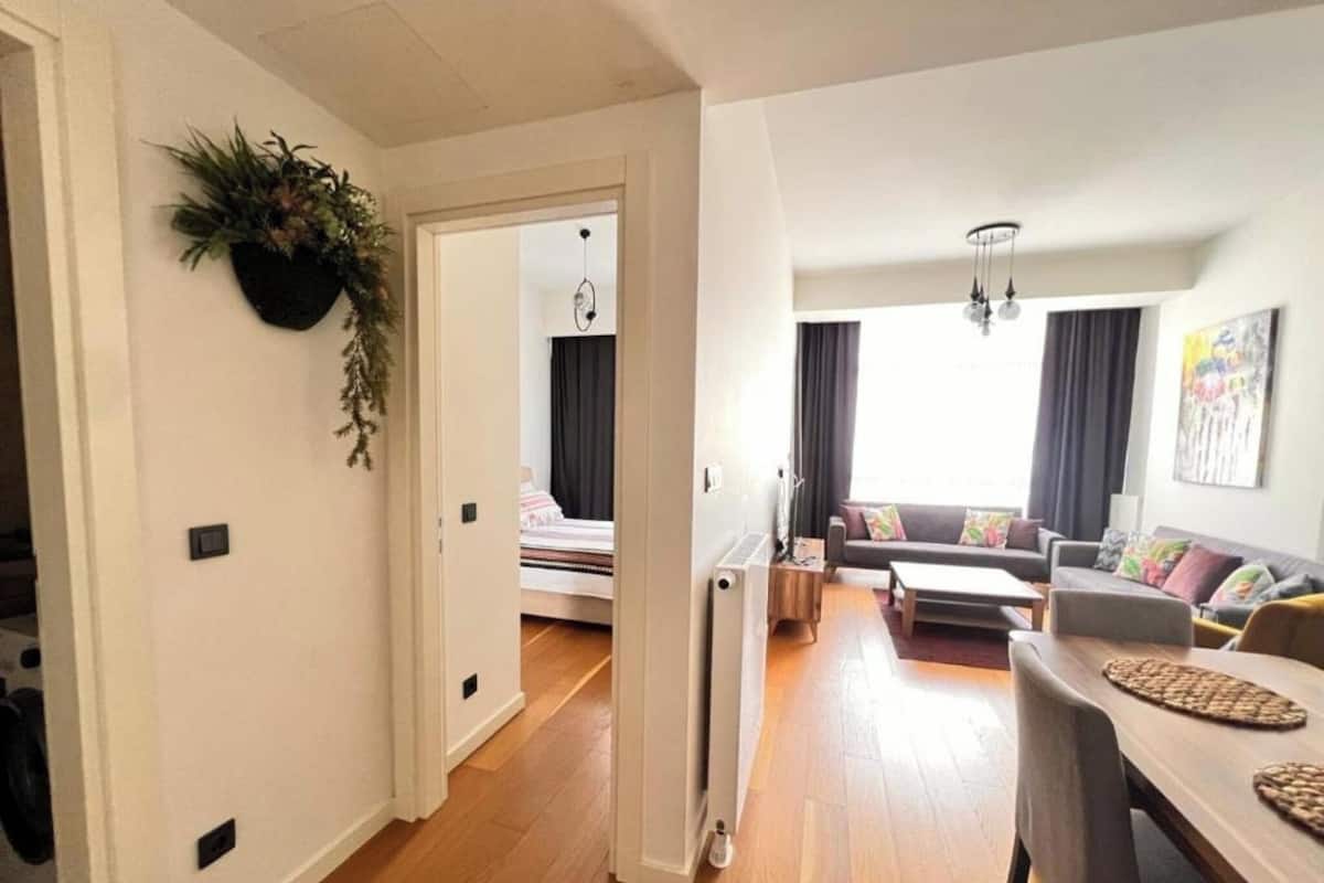 Ein modernes Wohnzimmer mit einer Couch, einem Esstisch und einem durch eine offene Tür einsehbaren Küchenbereich.