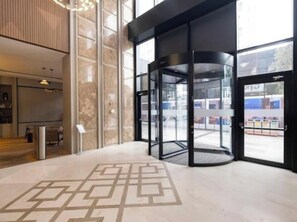 Una puerta giratoria con un diseño geométrico en el suelo, ventanas amplias y una decoración interior moderna.
