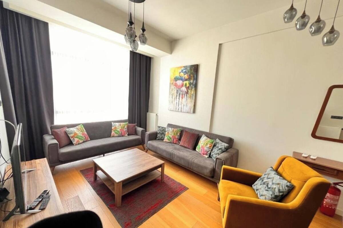 Ein Wohnzimmer mit einer Sofagarnitur, einem Couchtisch, einem gelben Sessel und einem Gemälde an der Wand.