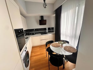 Una cocina moderna con horno integrado, una mesa de comedor con sillas y una lavadora.