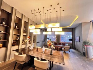 A modern dining area with a long table, multiple chairs, hanging pendant lights, and a sofa in the background. - G Tower Residence - Near Mimar Sinan Metro Station (Istanbul)