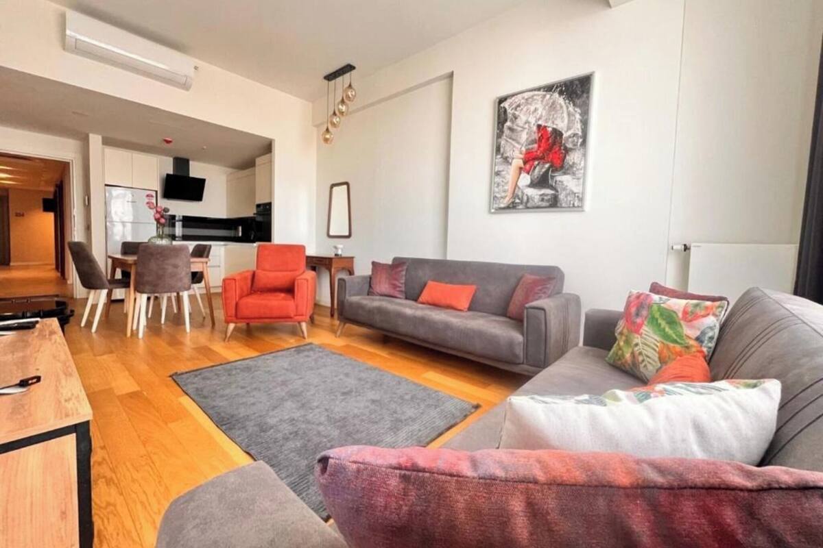 Ein modernes Wohnzimmer mit einem grauen Sofa, einem roten Sessel und einem Essbereich mit Tisch und Stühlen.