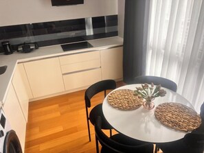 Una cocina compacta con armarios blancos, una encimera negra y una mesa redonda con individuales tejidos.