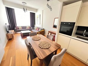 A modern apartment with a dining area, sofa set, kitchen, and a large window. - G Tower Residence - Near Mimar Sinan Metro Station (Istanbul)