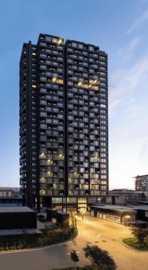 Un edificio de gran altura con varios pisos, una entrada central y un área ajardinada alrededor.