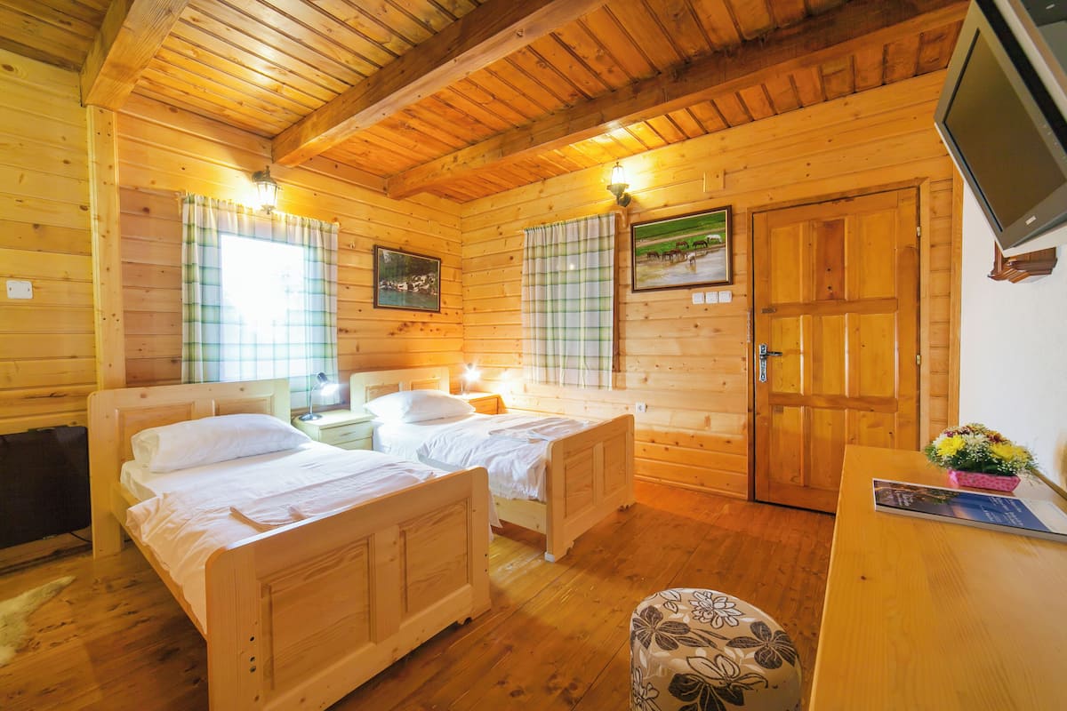 Una habitación de cabaña de madera con dos camas, un escritorio y un televisor montado en la pared.