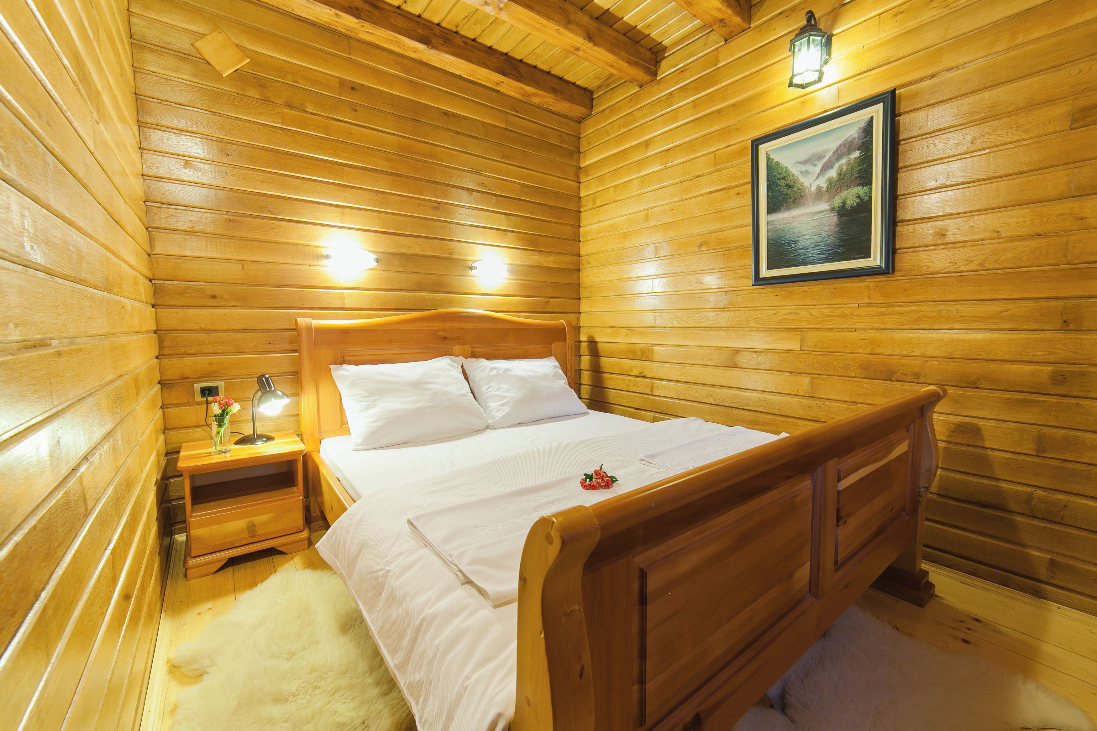 Una habitación de cabaña de madera con una cama, mesita de noche, lámpara y un cuadro enmarcado en la pared.
