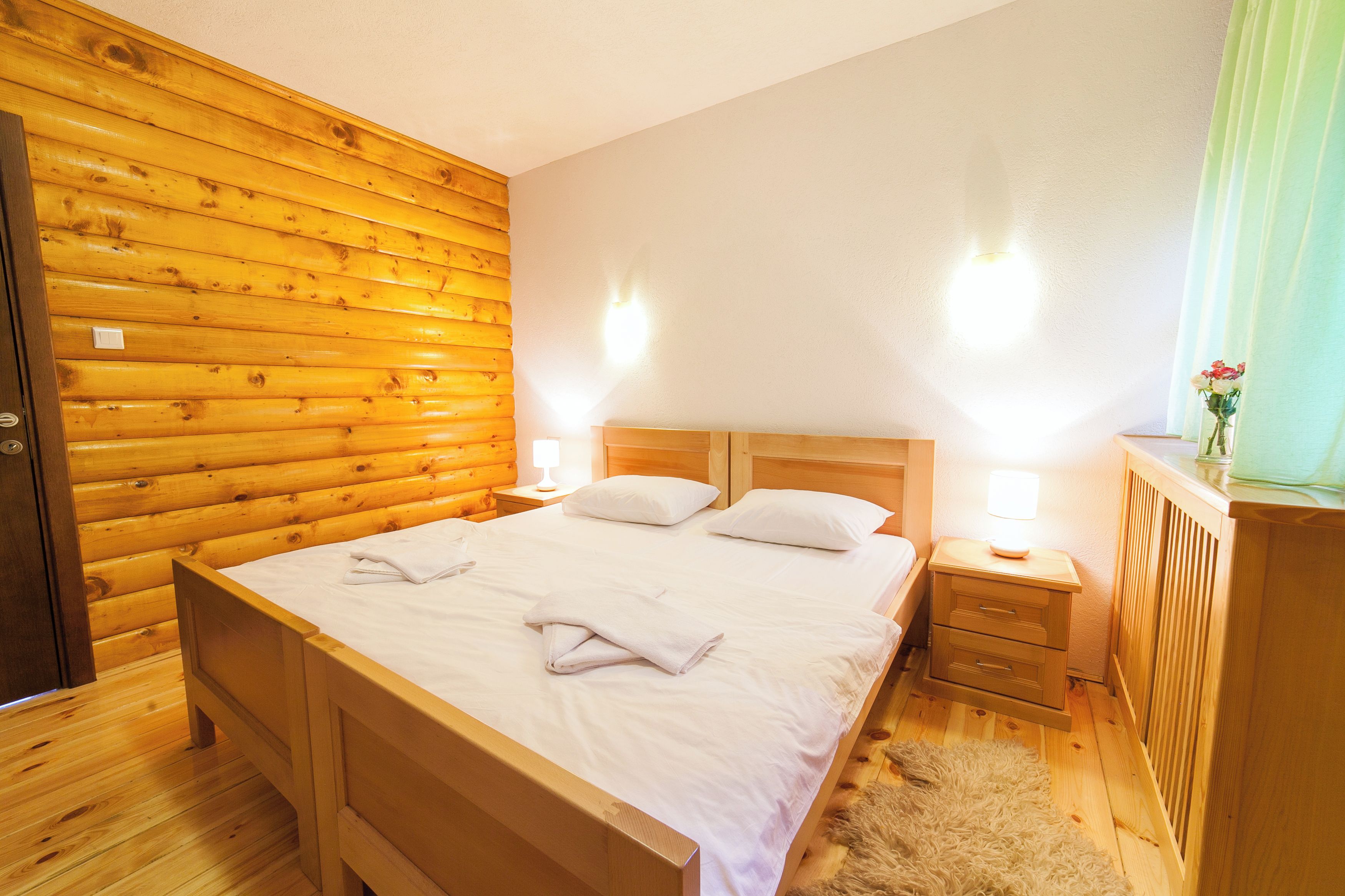 A wooden-paneled bedroom with a bed, two bedside tables, and a nightstand.