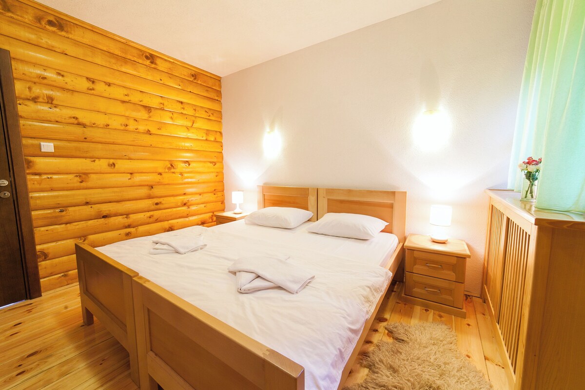 Un dormitorio con paneles de madera, una cama, dos mesitas de noche y un buró.