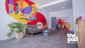 A modern co-living space with a large mural depicting co-living culture, a grey sofa, a coffee table, and a potted plant. - The Pad Co-living (Cebu City)