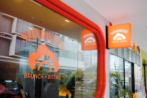 Restaurante con fachada de vidrio y señalización que indica que ofrece servicio de almuerzo tardío y estilo bistró.