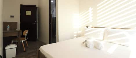 Una habitación de hotel con cama, escritorio, silla y un cubo de basura.