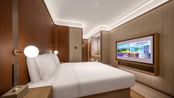 Quarto de hotel com cama grande, controles laterais, televisão fixada na parede e painel de parede em madeira.