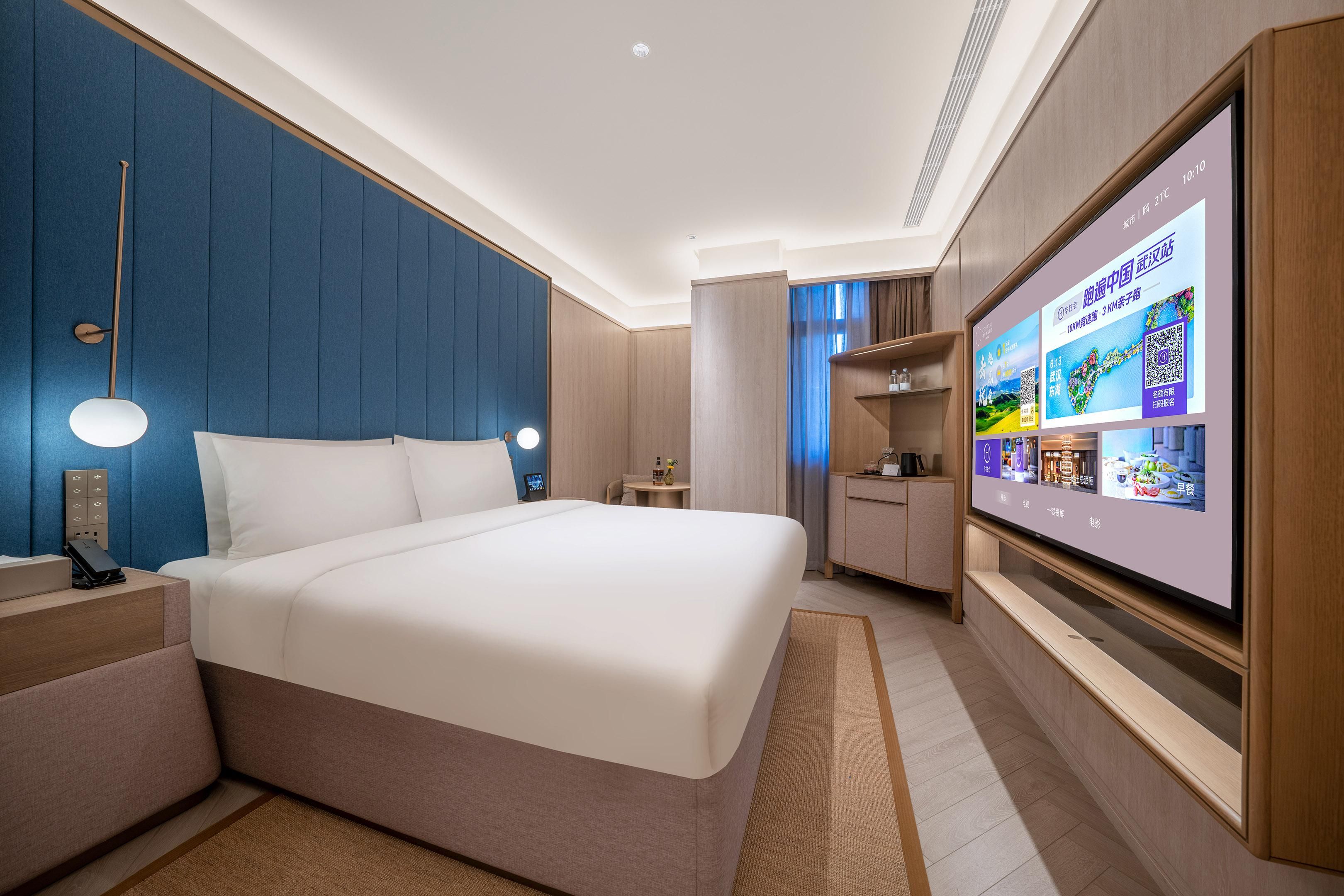 A modern hotel room with a large bed, bedside tables, a TV, and a wardrobe.