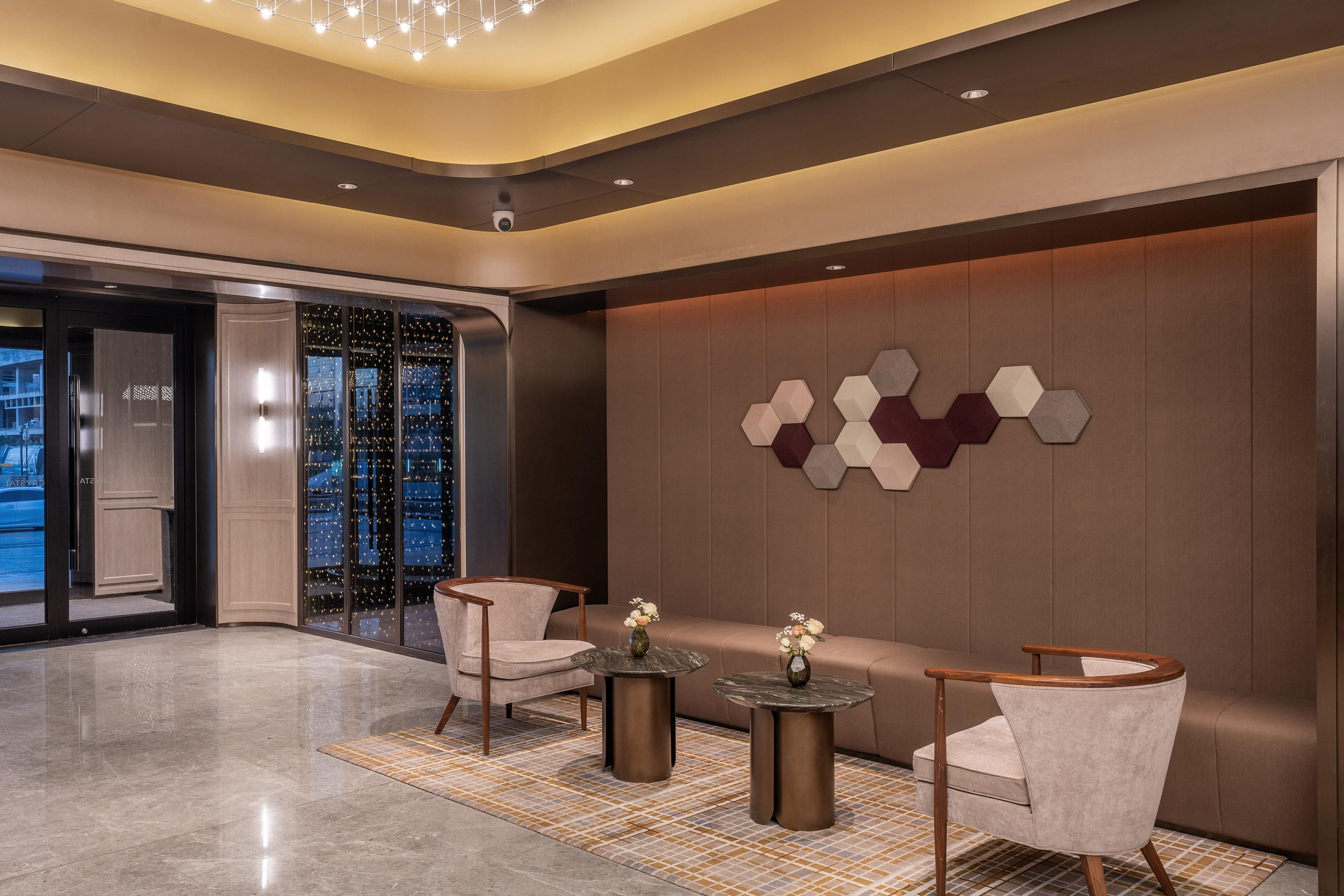 A modern lobby with a seating area, a wall with geometric patterns, and a glass door entrance.