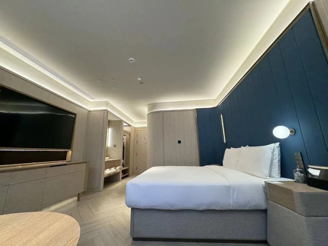 A modern hotel room with a bed, bedside table, TV, and built-in wardrobe.