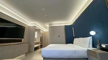 A modern hotel room with a bed, bedside table, TV, and built-in wardrobe.