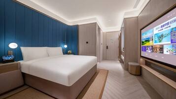 A modern hotel room with a large bed, bedside tables, a TV, and a wall-mounted screen displaying information.