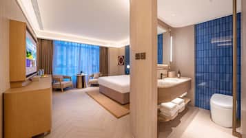 Habitación de hotel moderna con cama, escritorio, silla, televisor y baño con inodoro y lavamanos.