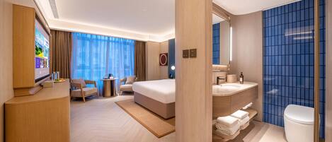 A modern hotel room with a bed, a desk, a chair, a TV, a bathroom with a toilet and sink.