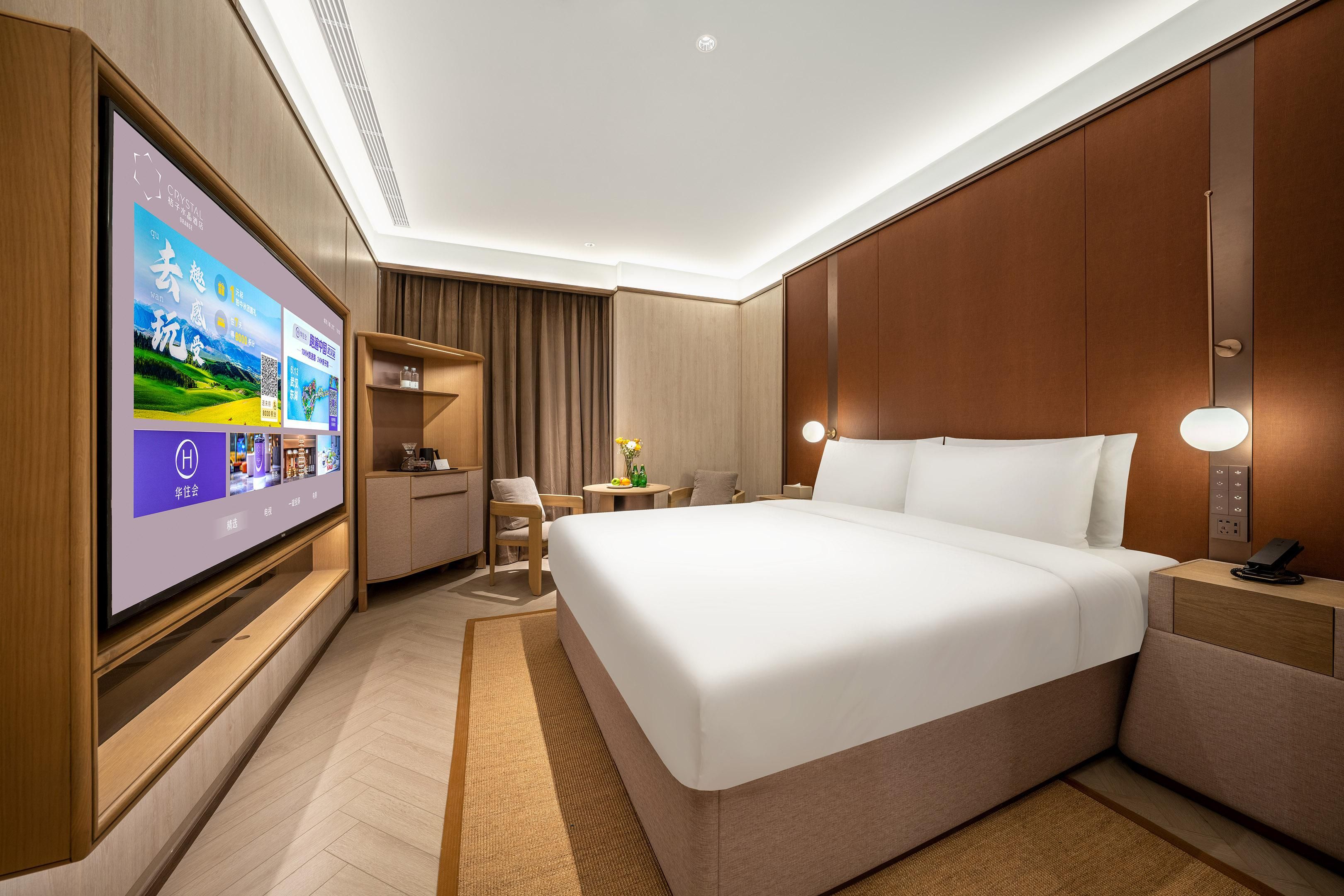 A hotel room with a large flat-screen TV, a bed, a desk, and a chair.