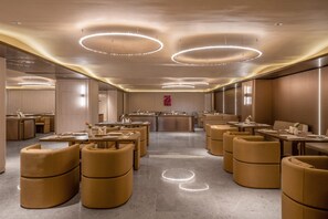 Un moderno vestíbulo de hotel con mesas redondas, asientos acolchados y un mostrador de recepción central.