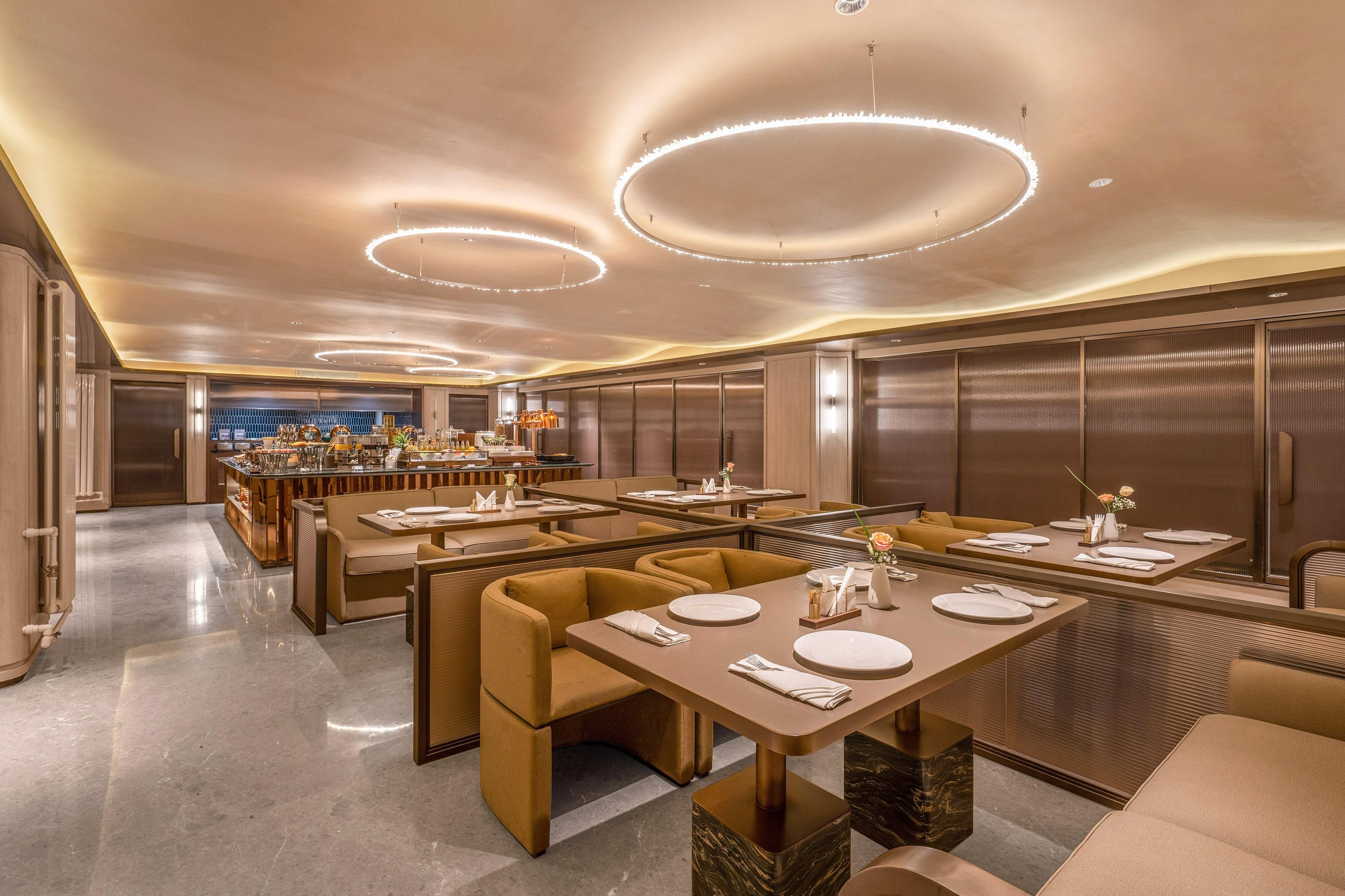 Ein modernes Restaurant mit mehreren Tischen, gepolsterten Sitzgelegenheiten und runden Deckenleuchten.