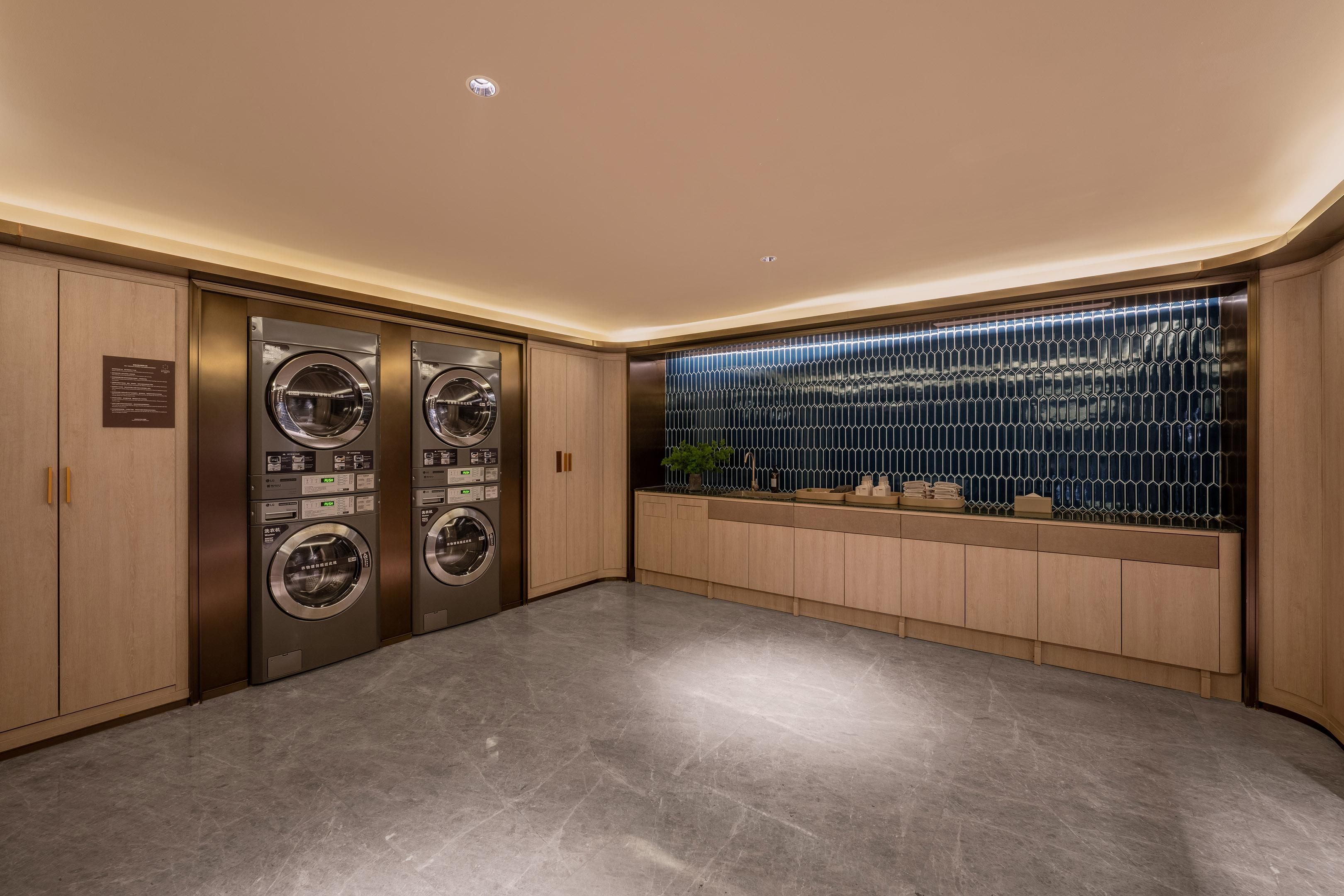 A modern laundry room with two stainless steel washers, wooden cabinets, and a decorative tiled wall.