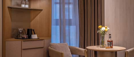 A hotel room with a bed, a desk with a coffee maker, a bottle, and a vase with flowers.