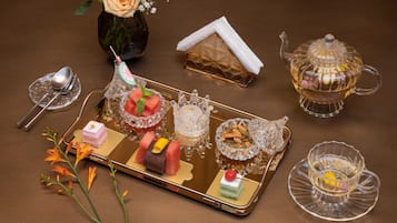 A tray with various desserts, a teapot, and a vase with flowers on a table.