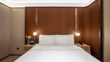 Quarto de hotel com uma cama grande, paredes de painel de madeira, mesa de cabeceira com telefone e relógio digital.