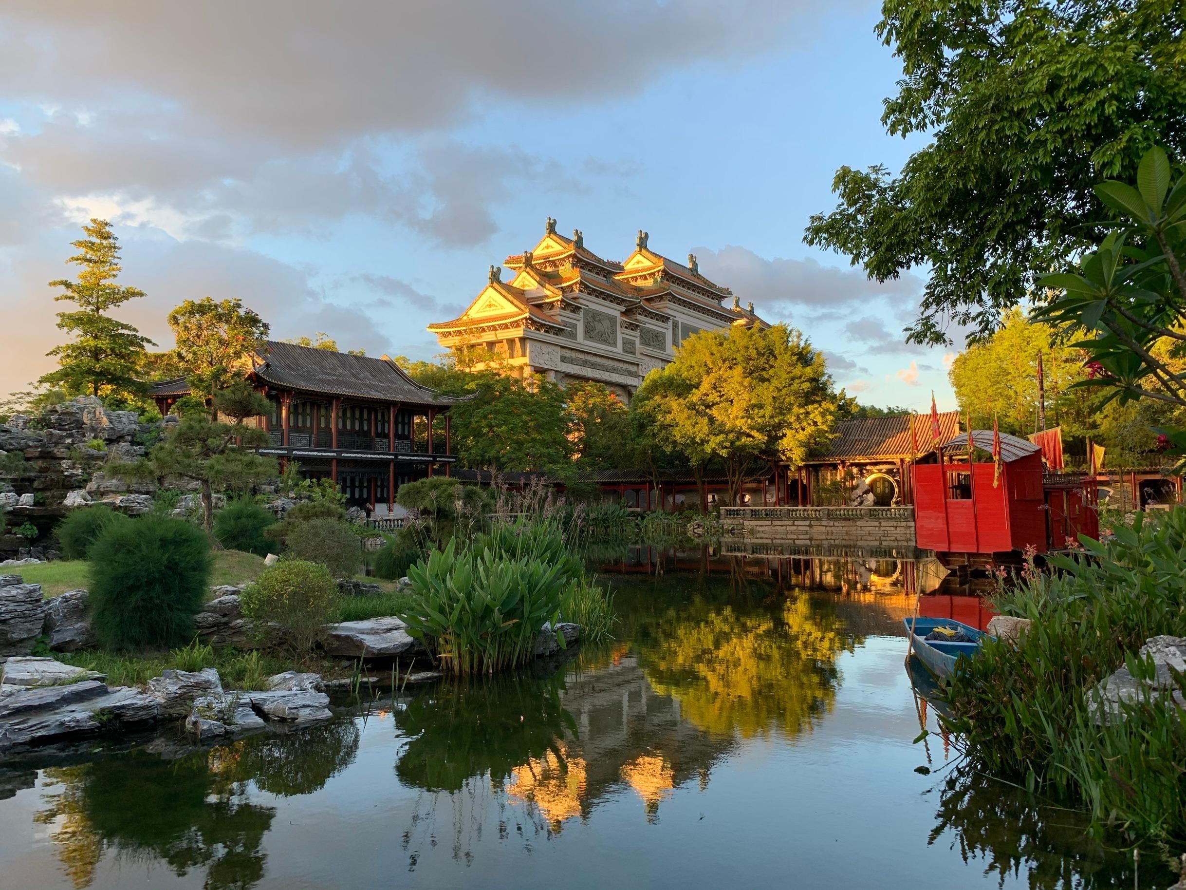 A traditional building with a reflection in the water, surrounded by greenery and a small bridge.