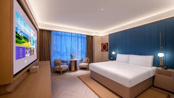 A hotel room with a large bed, a TV, a small table with chairs, and a view of the outdoors through the window.