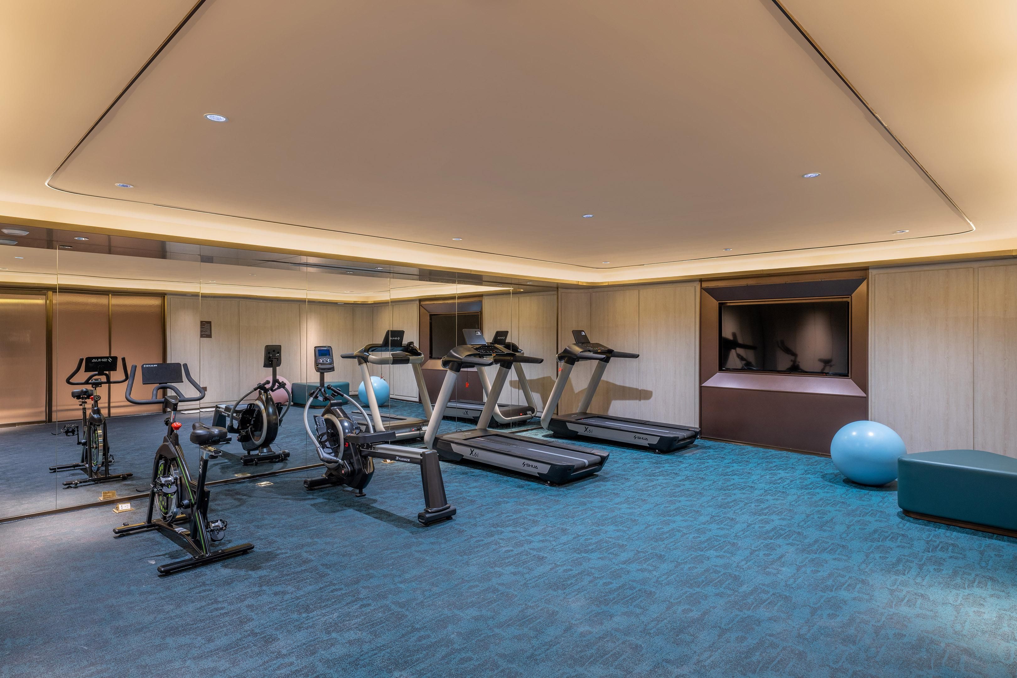 A gym with treadmills, stationary bikes, and exercise balls.