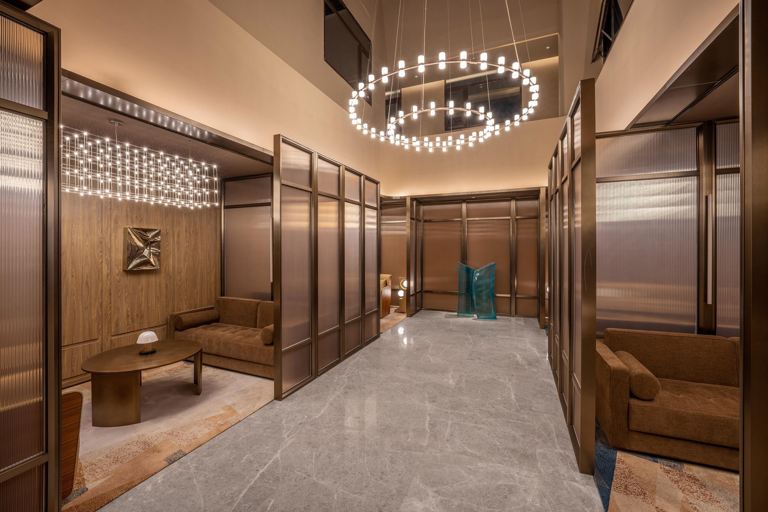 A modern hotel lobby with a marble floor, a round chandelier, and a seating area with a sofa and a coffee table.