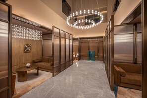 Eine moderne Hotelhalle mit Marmorboden, einem runden Kronleuchter und einer Sitzecke mit Sofa und Couchtisch.