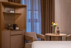 A hotel room with a bed, a small table with a bottle and flowers, a chair, a shelf with bottles, and a window with curtains. - Crystal Orange Hotel Beijing Yizhuang JD (Beijing)